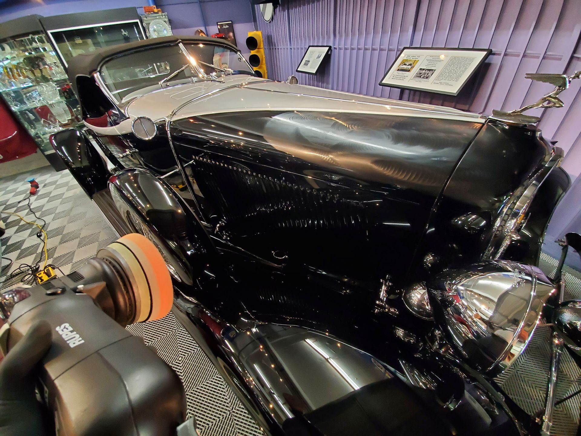 A person buffing a shiny black vintage car in a museum.