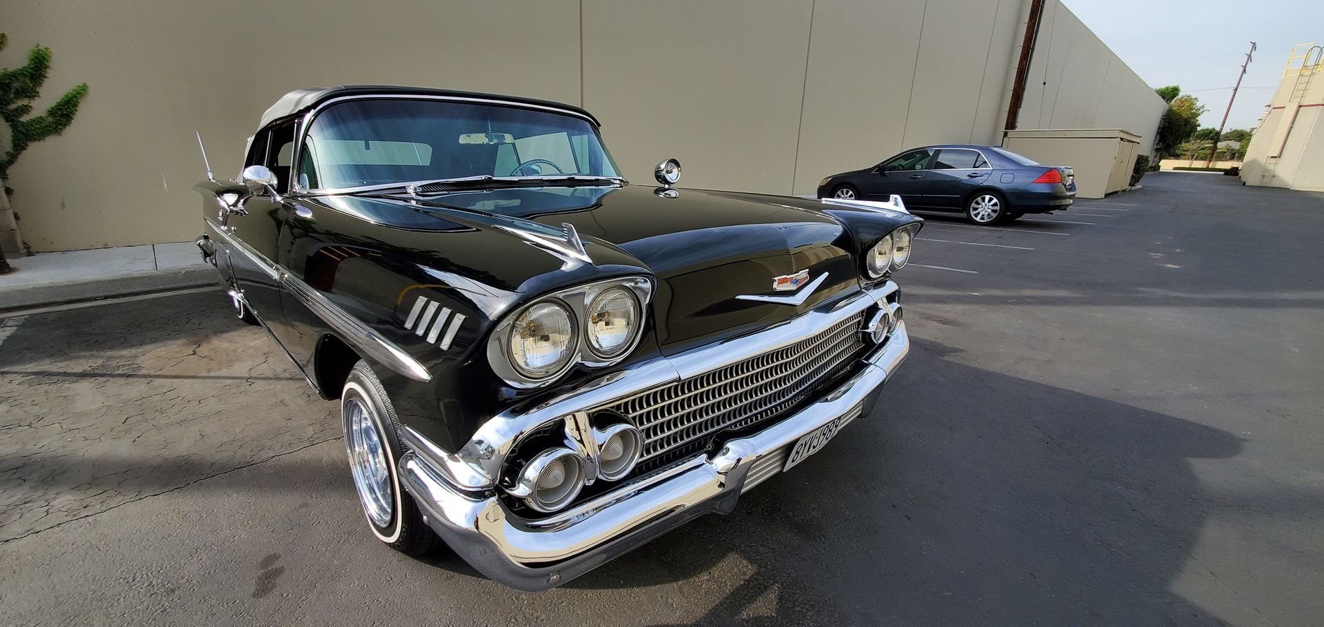 A black classic car parked in front of a building. A second car is parked in the background.