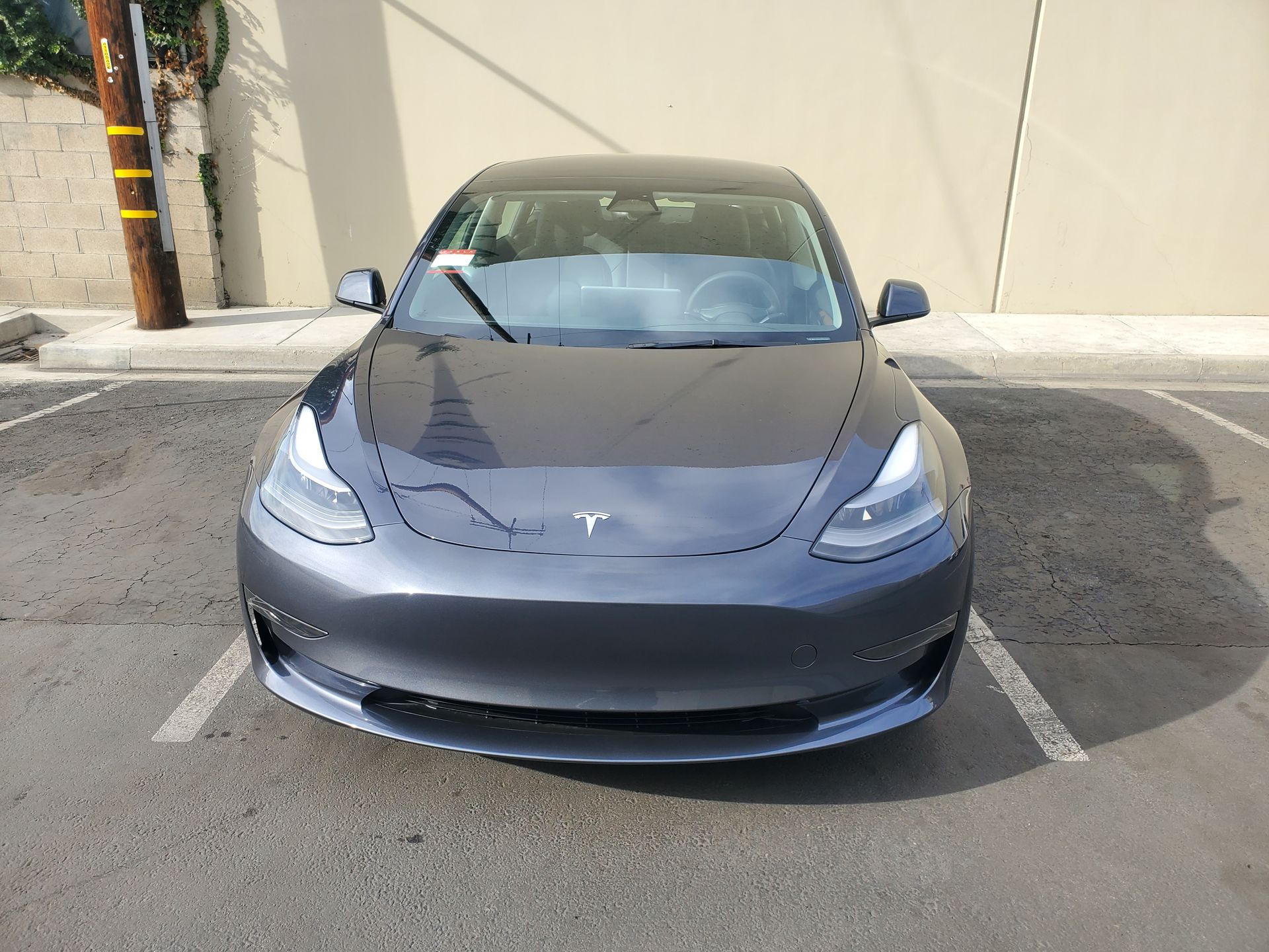 Gray Tesla car parked in a parking lot, facing forward.