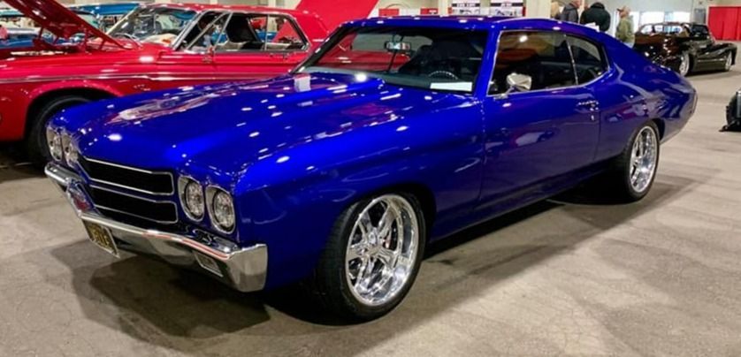 A bright blue Chevrolet Chevelle at a car show, displaying chrome wheels and shiny paint.