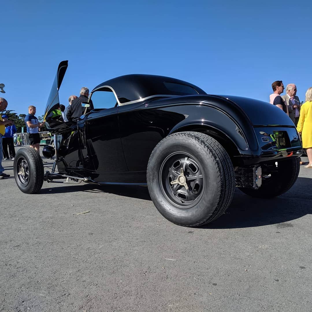 Black hot rod with gullwing doors on asphalt, people in the background.