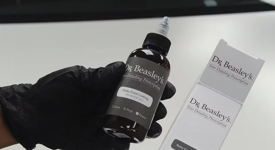 Person in black glove holding Dr. Beasley's paint coating bottle and its box on a white surface.