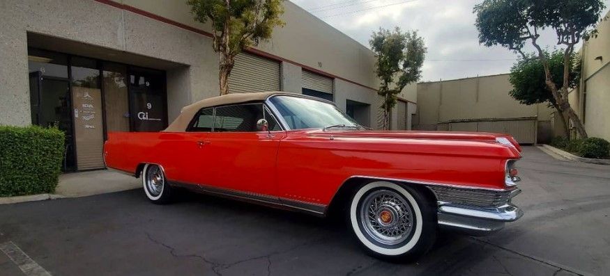 Red convertible car parked in front of a building with a beige top and white-walled tires.