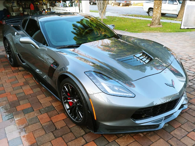 Gray Corvette Z06 sports car parked on a brick driveway. Red brake calipers visible.