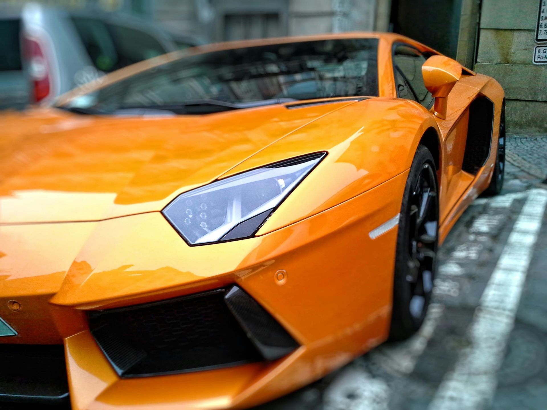Bright orange Lamborghini parked on the street, black wheels, angled headlights.
