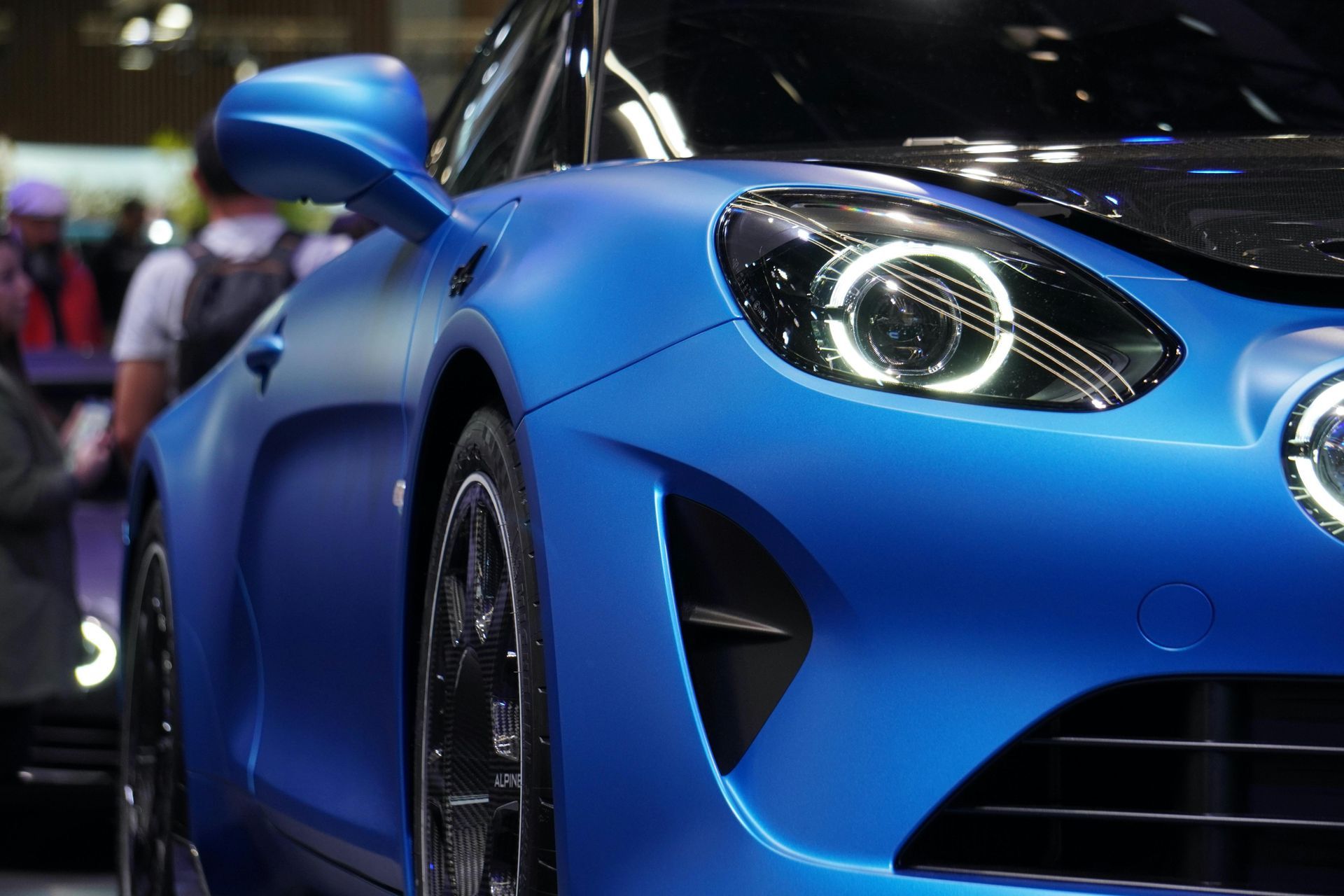 Blue Alpine sports car, close-up. Headlight detail visible, matte finish, side mirror.