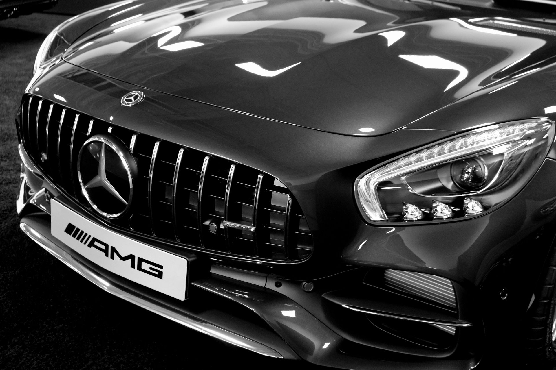 Black and white close-up of a Mercedes-AMG sports car, showing the front grill, logo, and headlight.