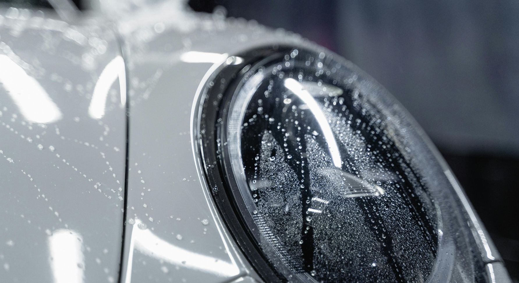 Car headlight being washed; soap and water on white car body.