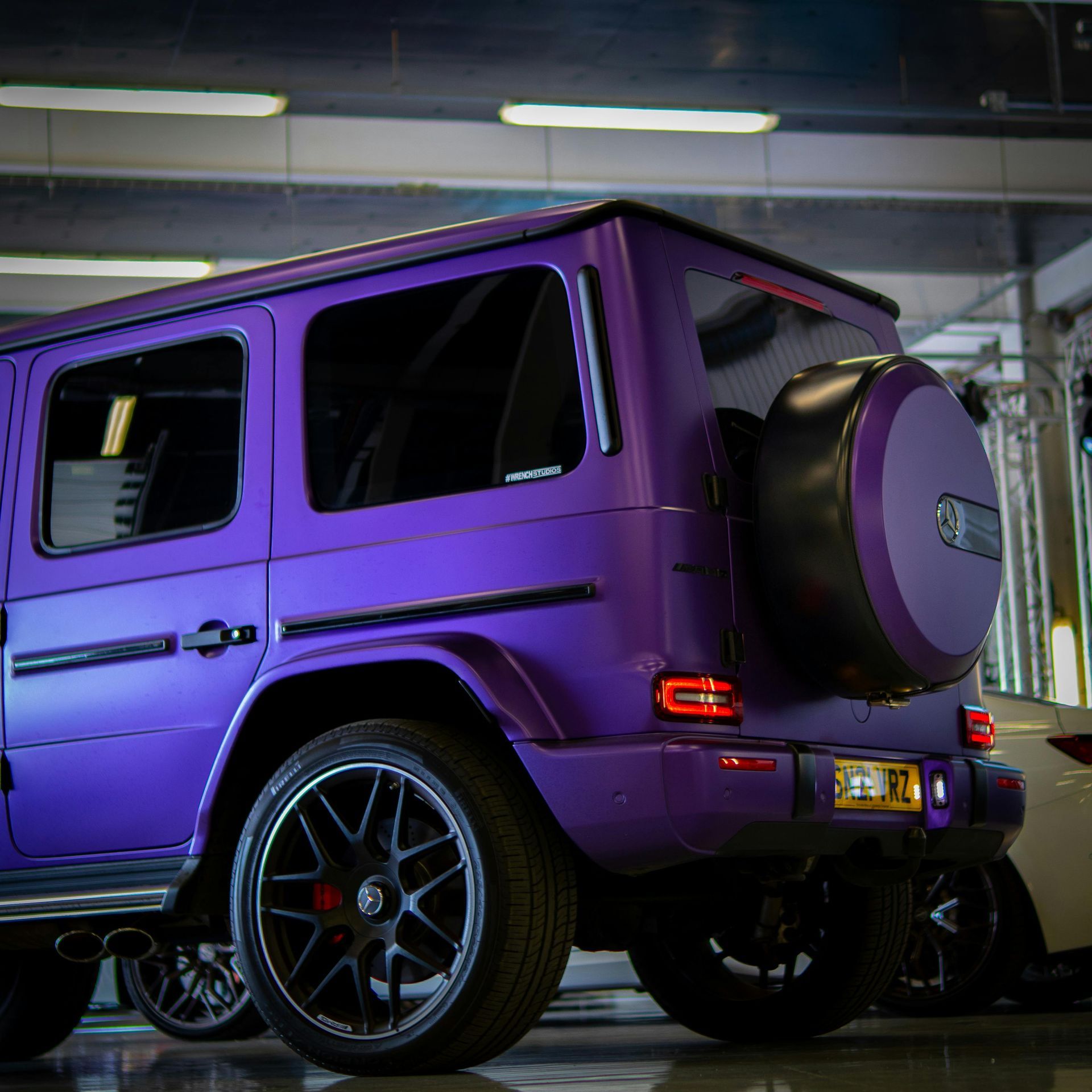 Purple Mercedes G-Wagon, spare tire on back, black wheels, parked indoors.