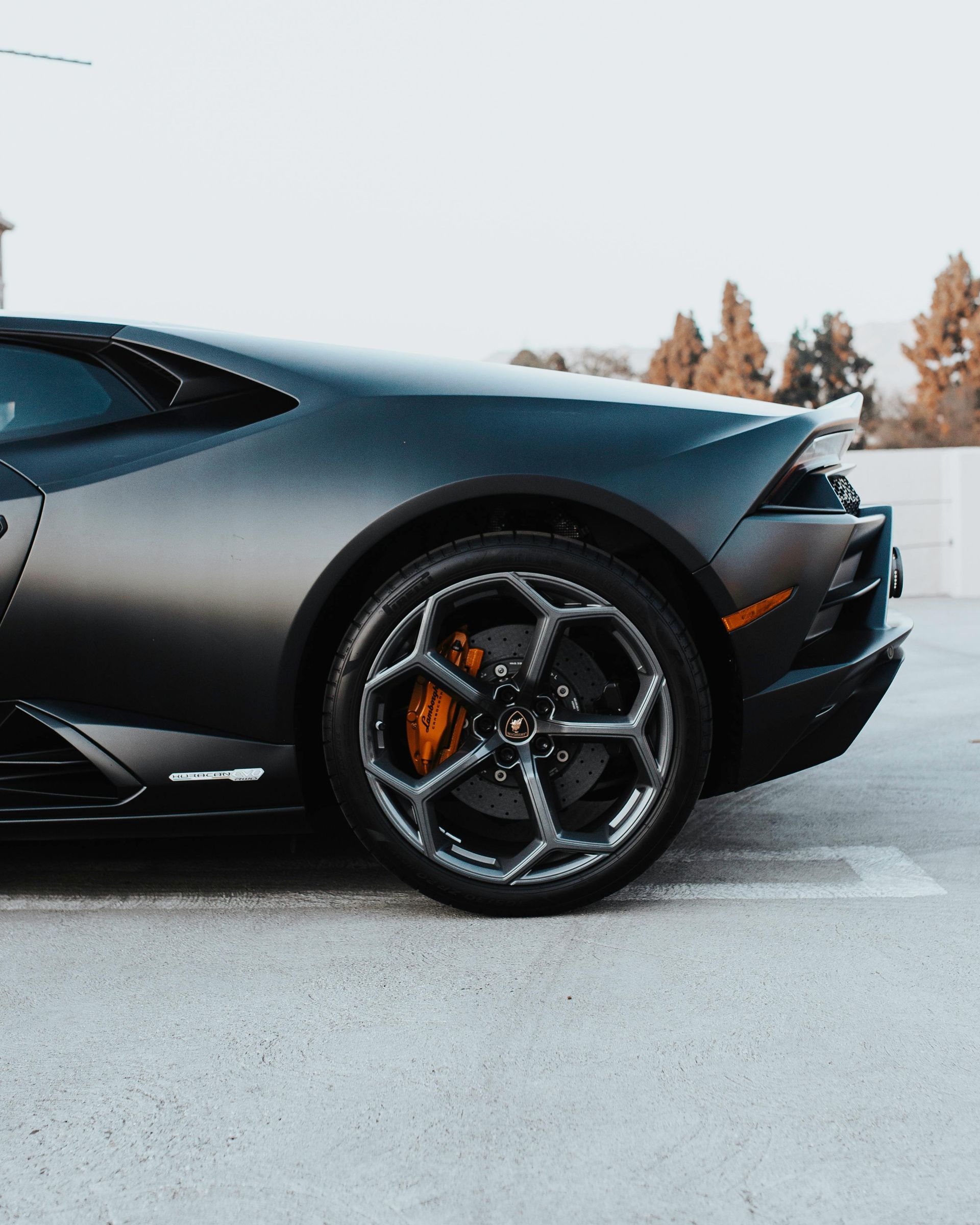 Black Lamborghini car with orange brake calipers, parked on concrete.