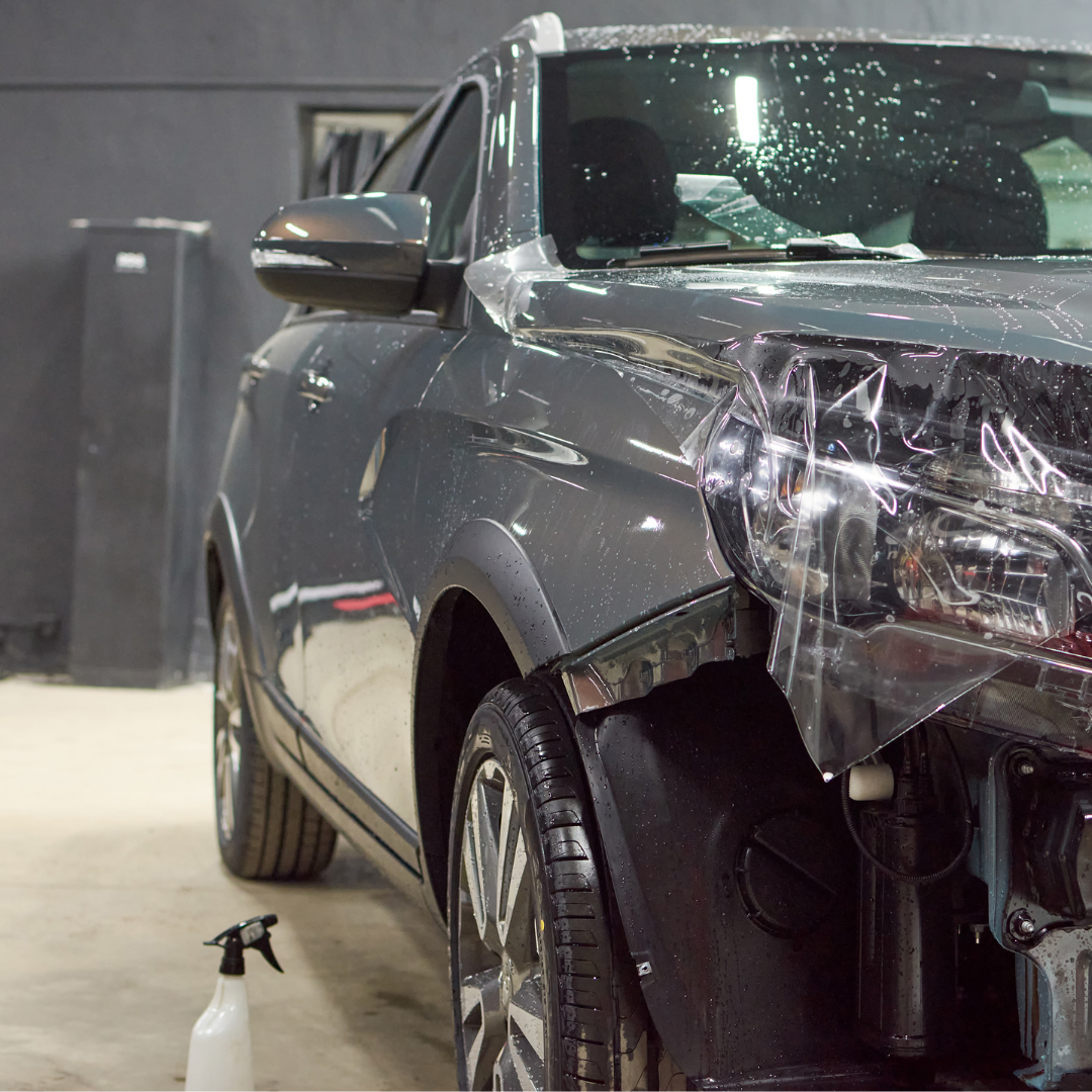 Gray car with protective film applied to front, in a workshop.