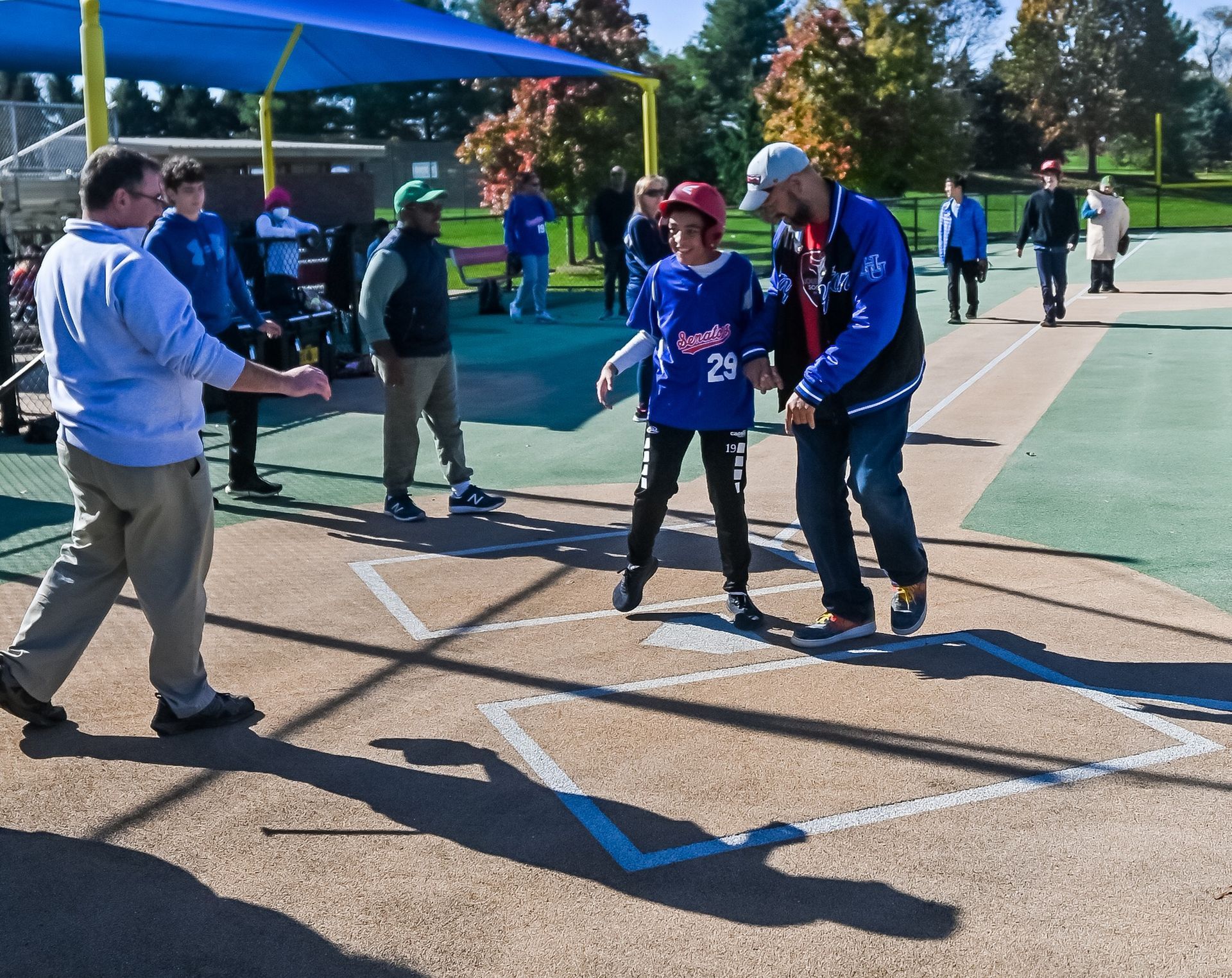 Miracle League player running into home base with buddy volunteers 