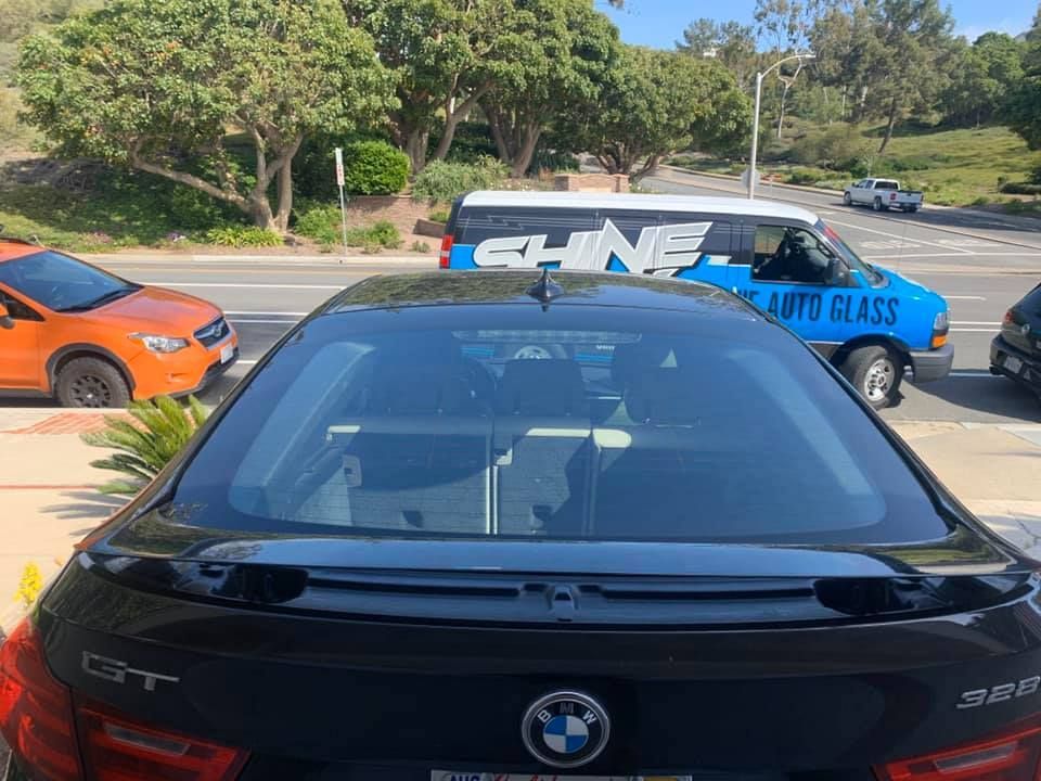 A black bmw is parked in front of a van that says auto glass.