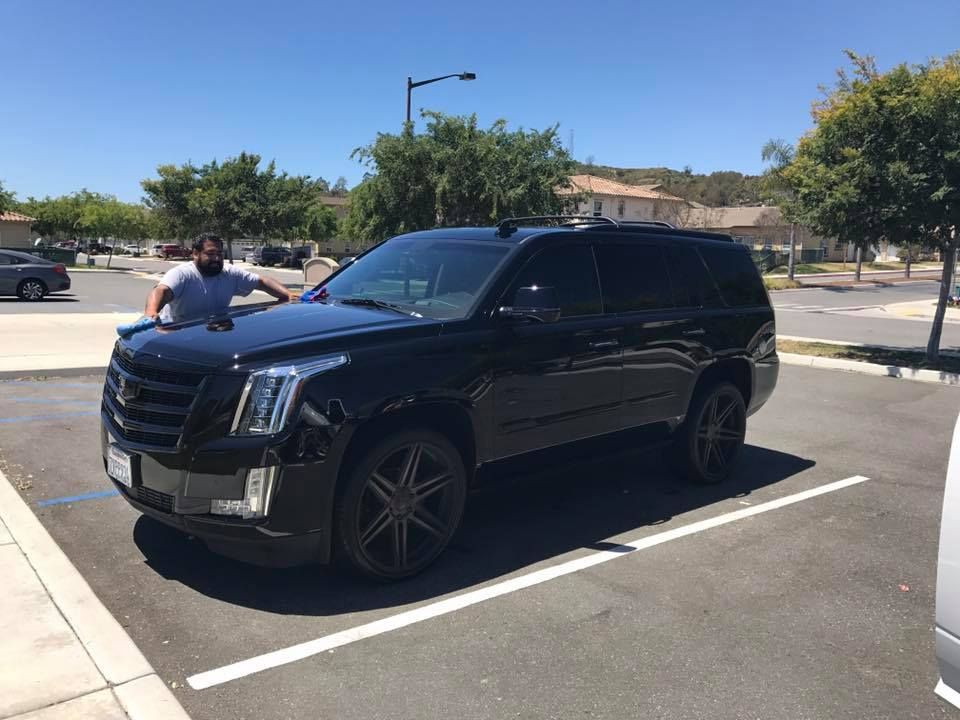 A man is standing next to a black cadillac in a parking lot.