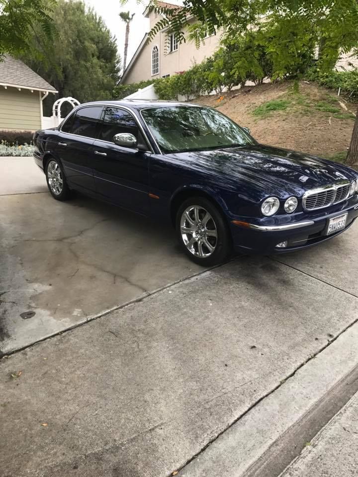 A blue jaguar x type is parked in a driveway next to a house.