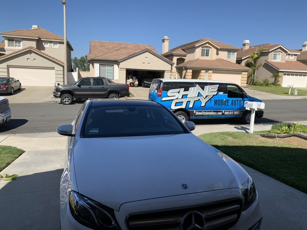 A white car is parked in front of a shine city van