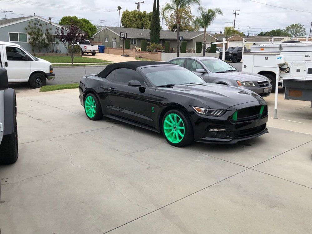 A black mustang with green wheels is parked in a parking lot.