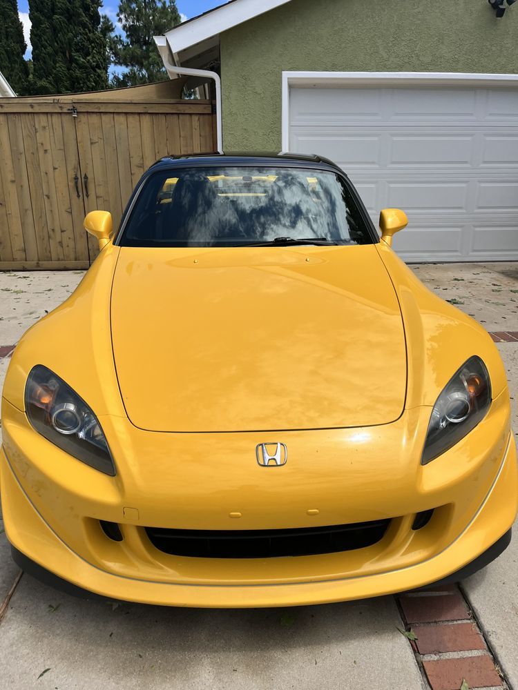 A yellow honda s2000 is parked in front of a garage door
