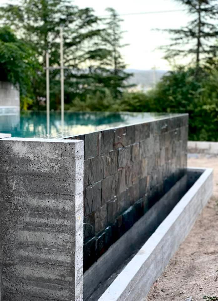 Fuente de agua de hormigón con piscina y árboles al fondo.