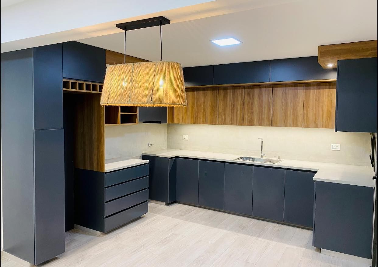 Cocina moderna con gabinetes azul marino, detalles de madera clara y una lámpara tejida.