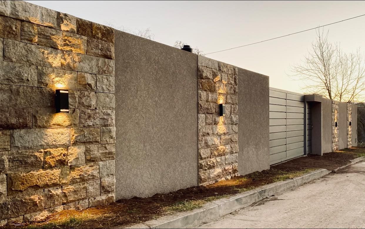 Valla de piedra y hormigón con aplique de iluminación junto a una carretera.