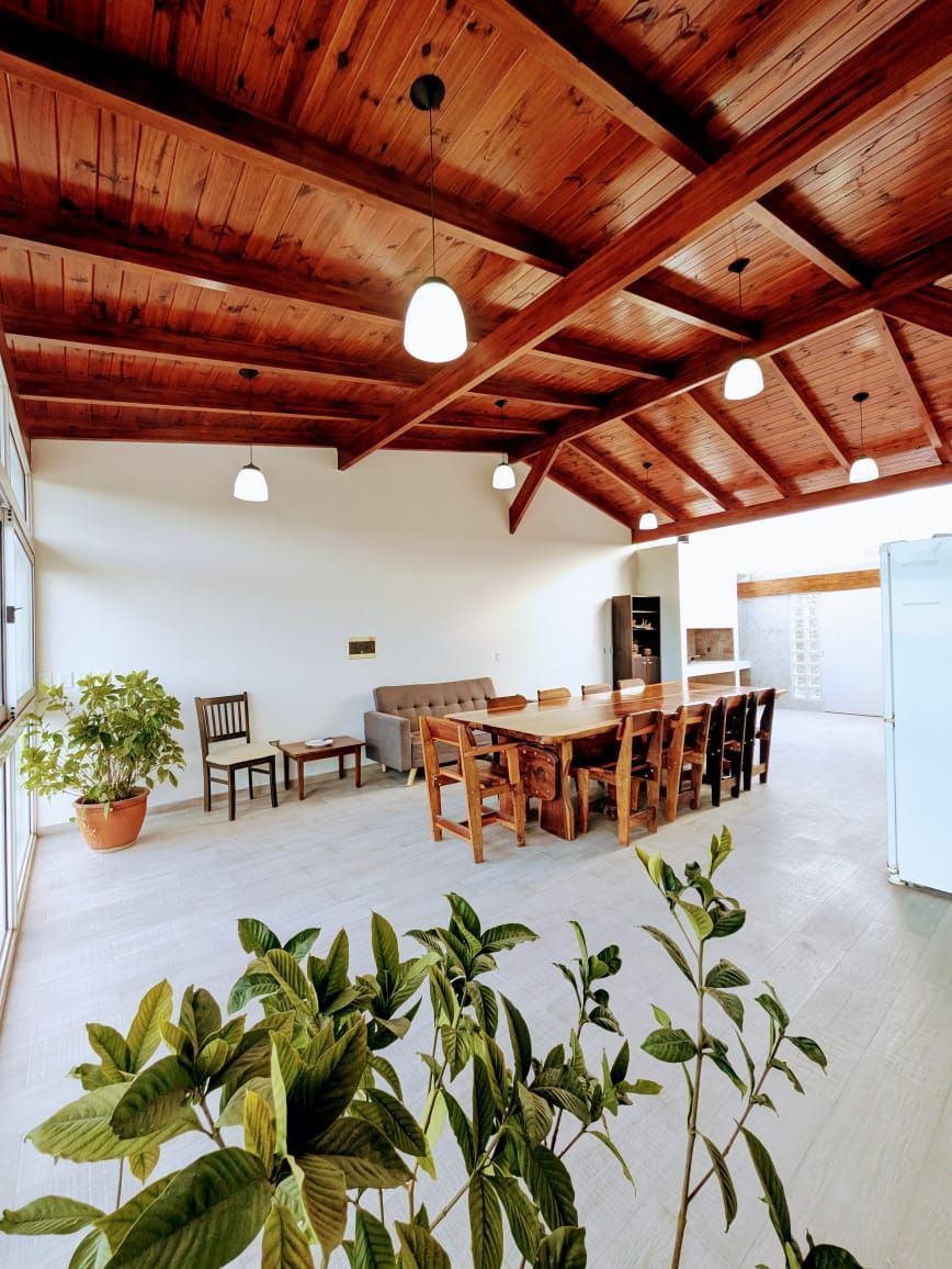 Una habitación grande y abierta con techo de madera, una mesa larga de madera y varias plantas.