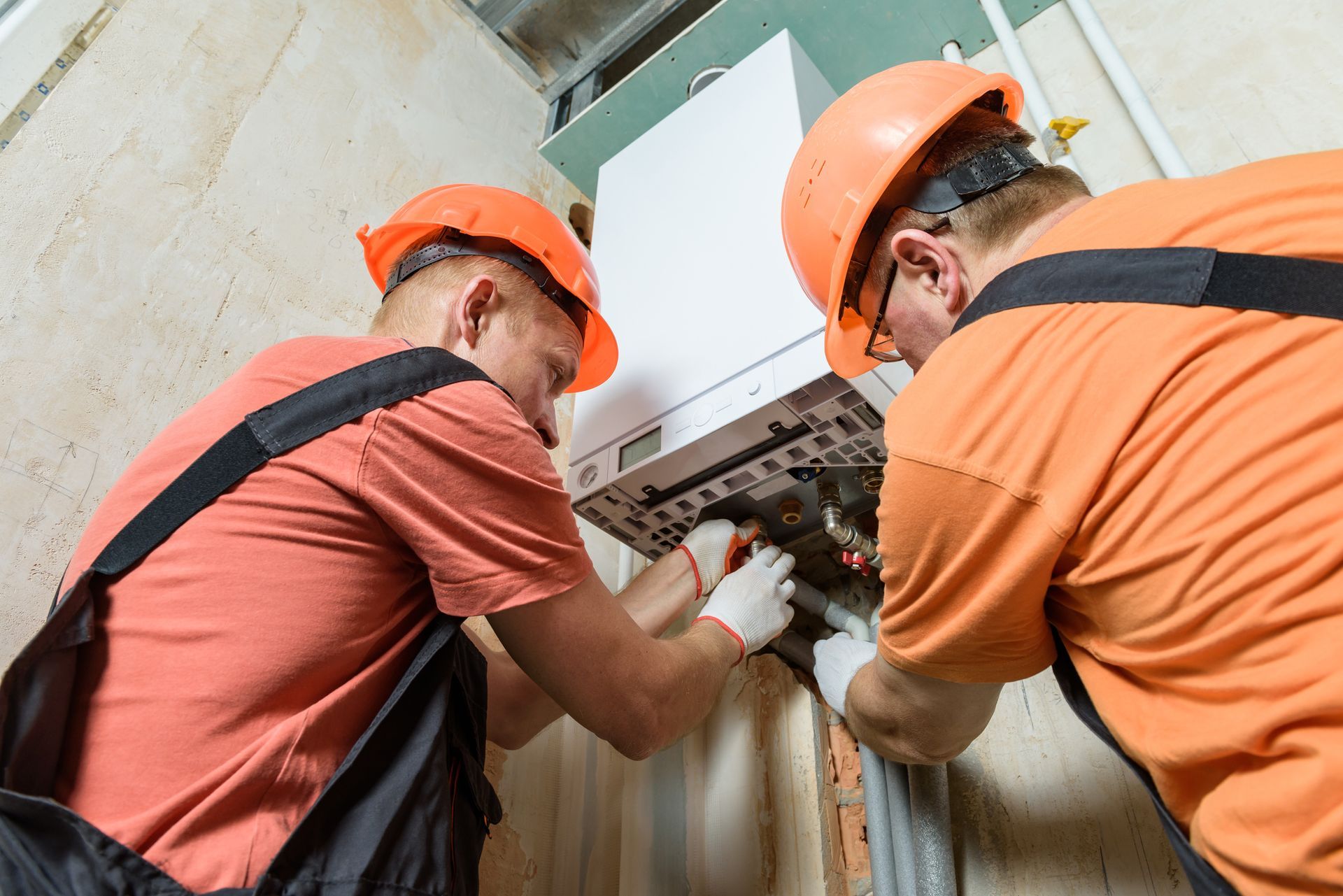 Two men are working on a boiler on a wall.