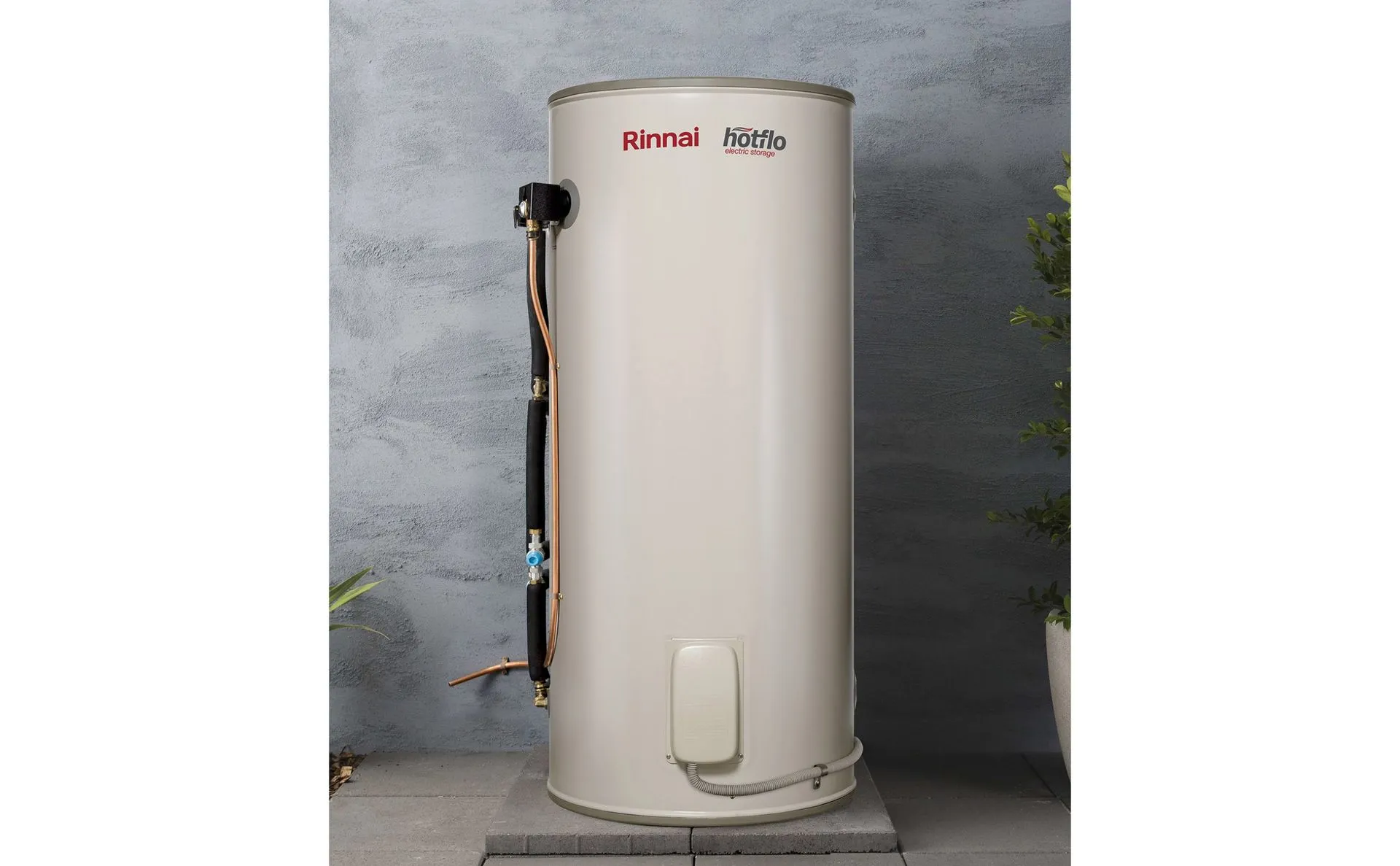 A tall, beige Rheem electric water heater outdoors on a concrete slab.