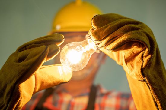 a man wearing gloves is holding a light bulb in his hands .