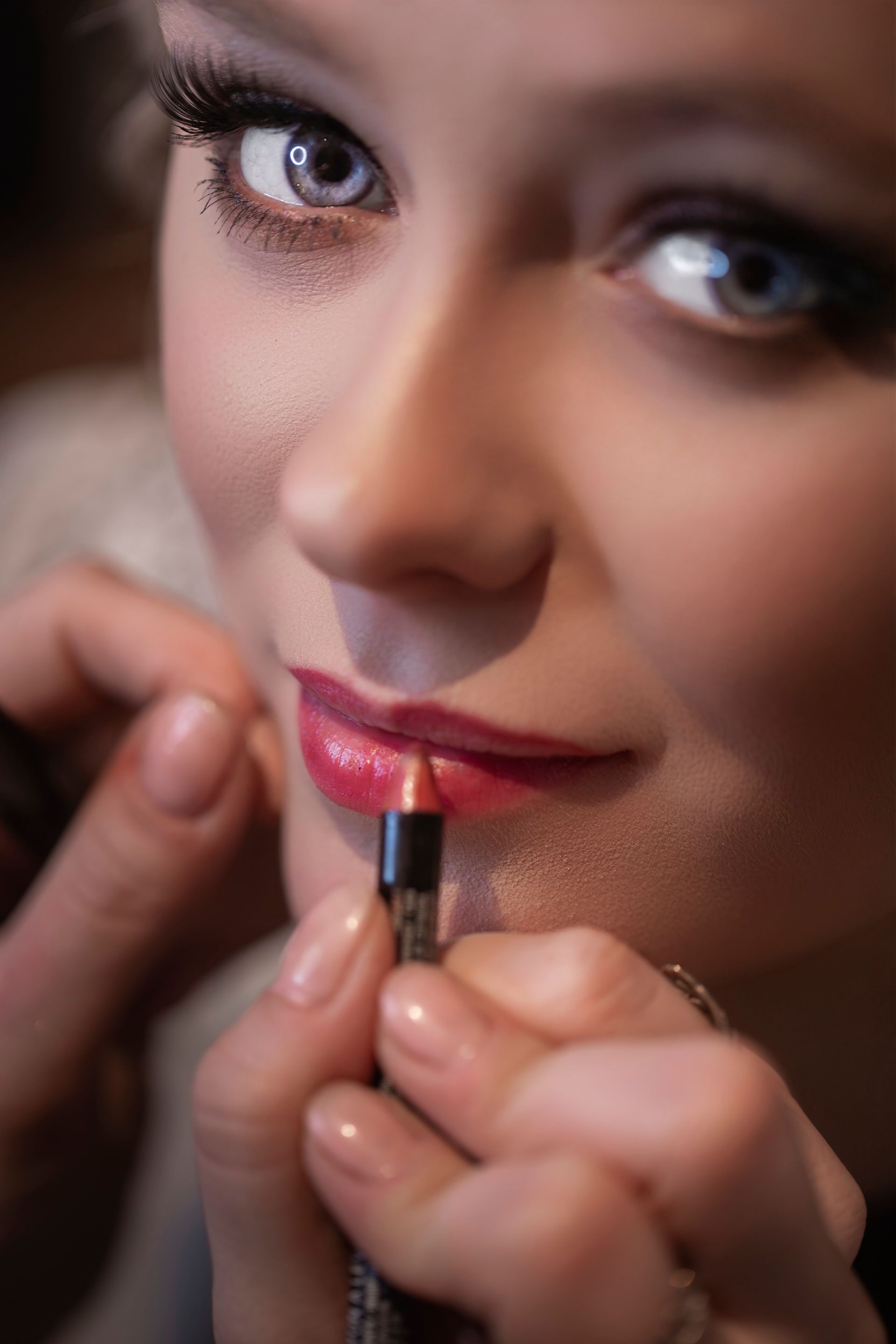 Makeup artist applying lipstick on a person with light eyes; close-up view.