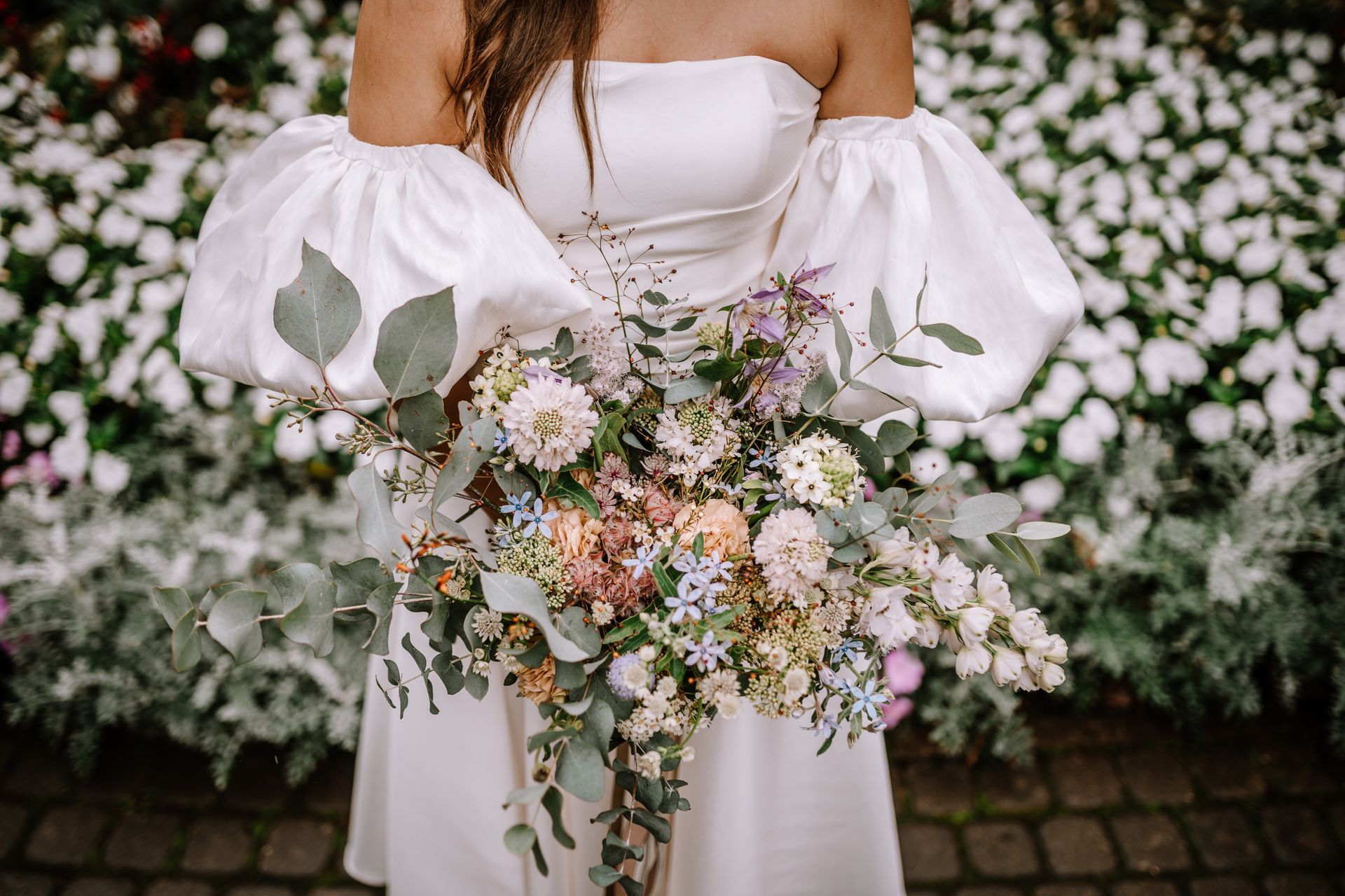 Woman in white dress holding colorful cascading bouquet.