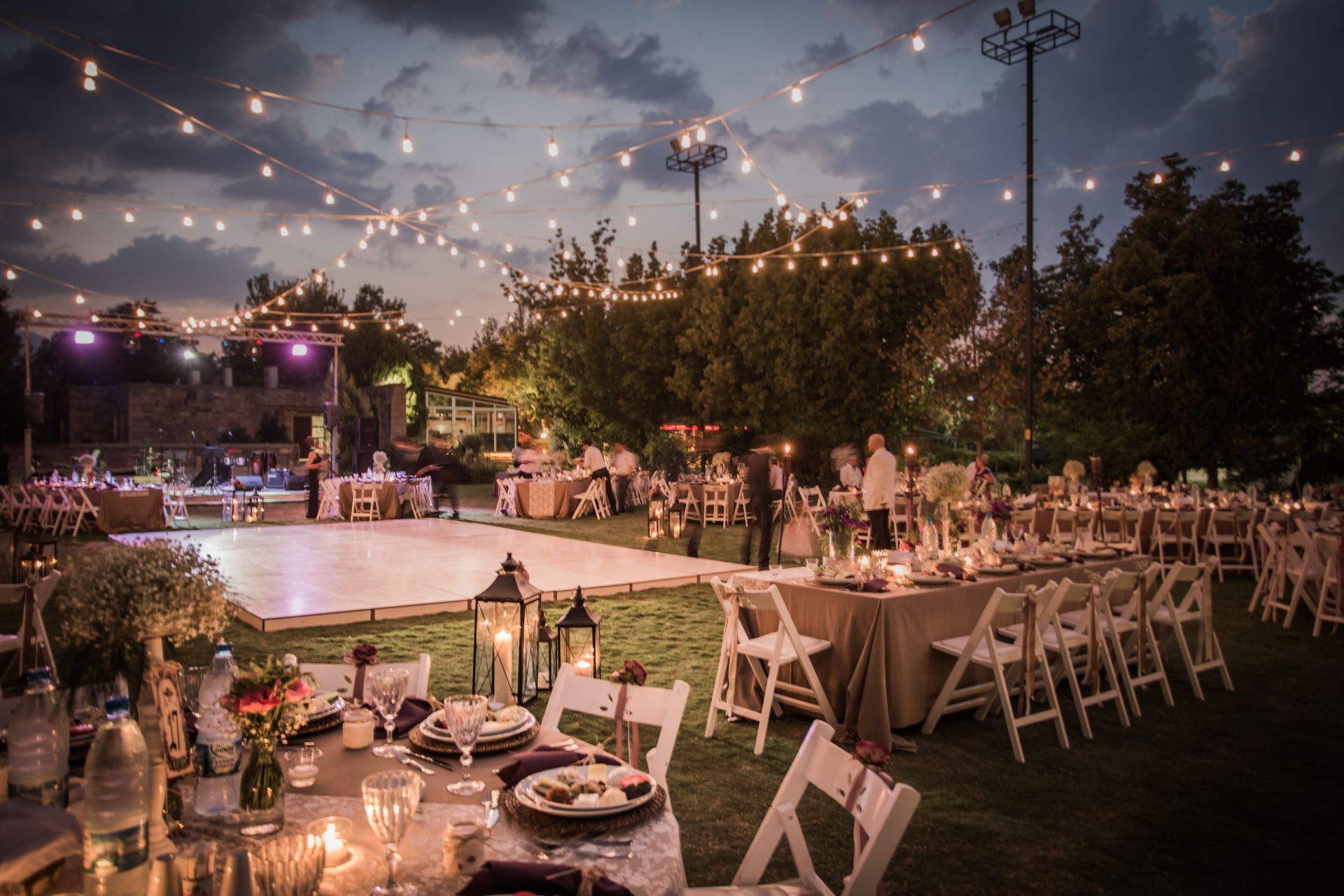 Outdoor wedding reception at dusk with string lights, tables, and a dance floor.