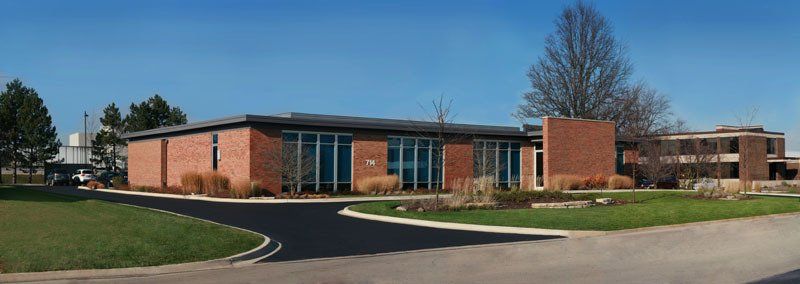 A large brick building with a lot of windows is surrounded by grass and trees.