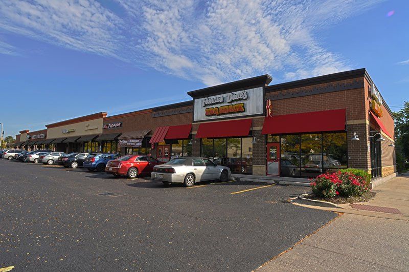 A row of cars are parked in front of a brick building with red awnings.