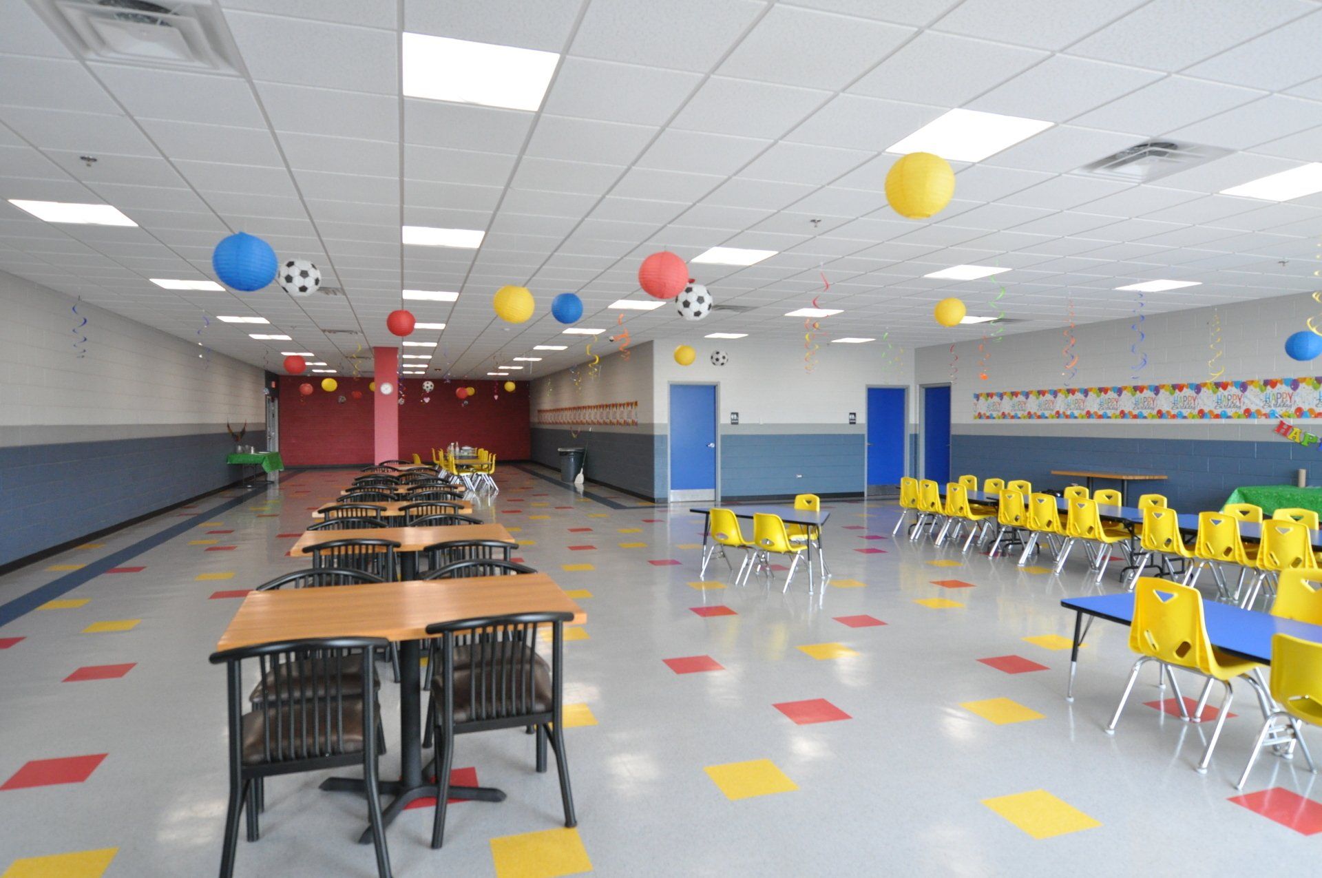 A large room with tables and chairs and balloons hanging from the ceiling.