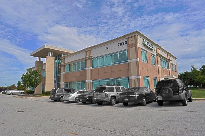 A row of cars are parked in front of a large building.