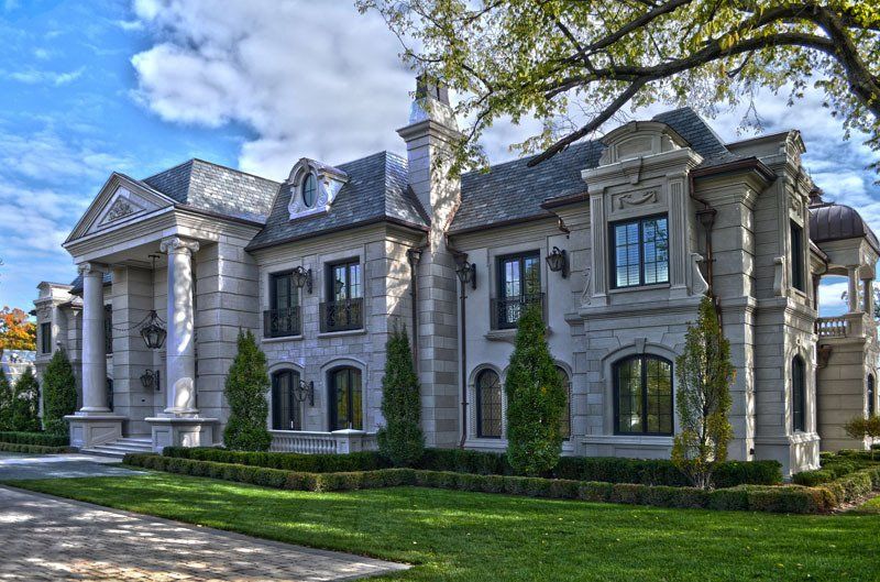 A large white house with a lot of windows is sitting on top of a lush green lawn.