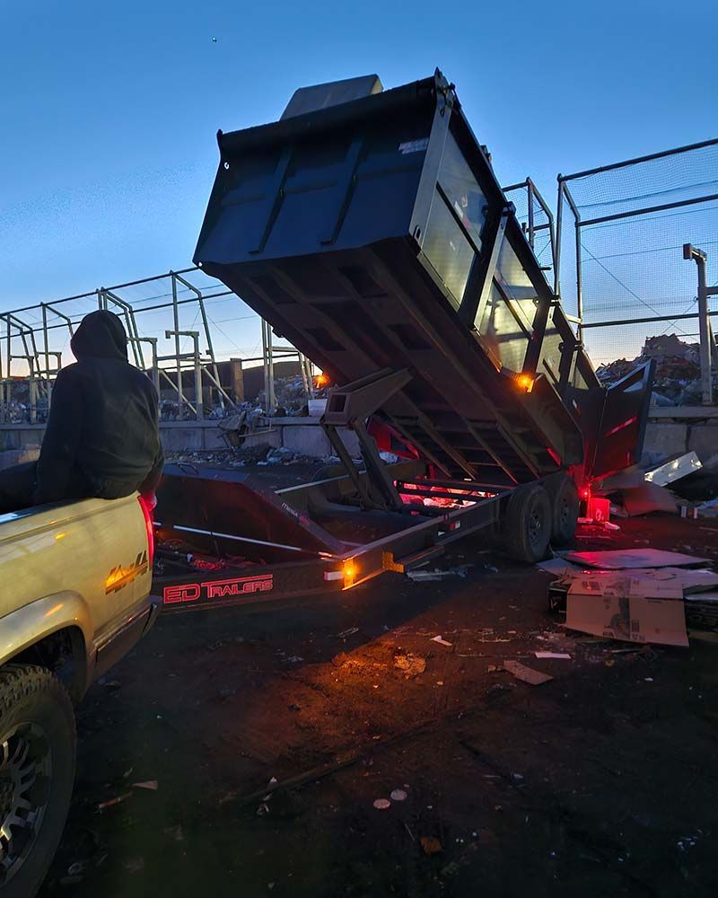 A man is sitting in the back of a truck next to a dumpster.