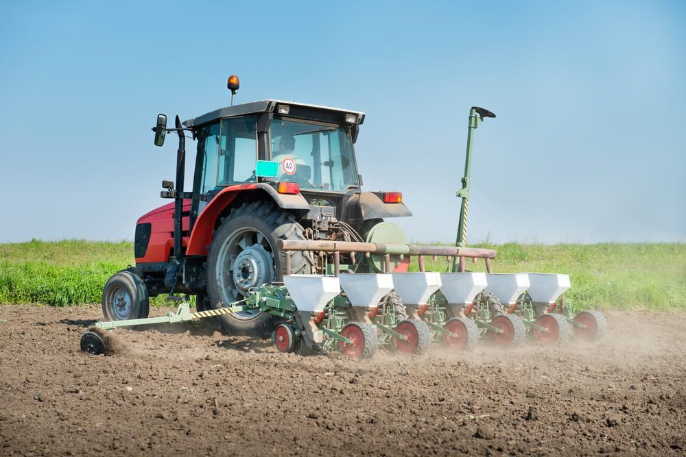 A Red Tractor is Ploughing a Field With a Planter Attached to It — Lavington Auto Electrical in Holbrook, NSW