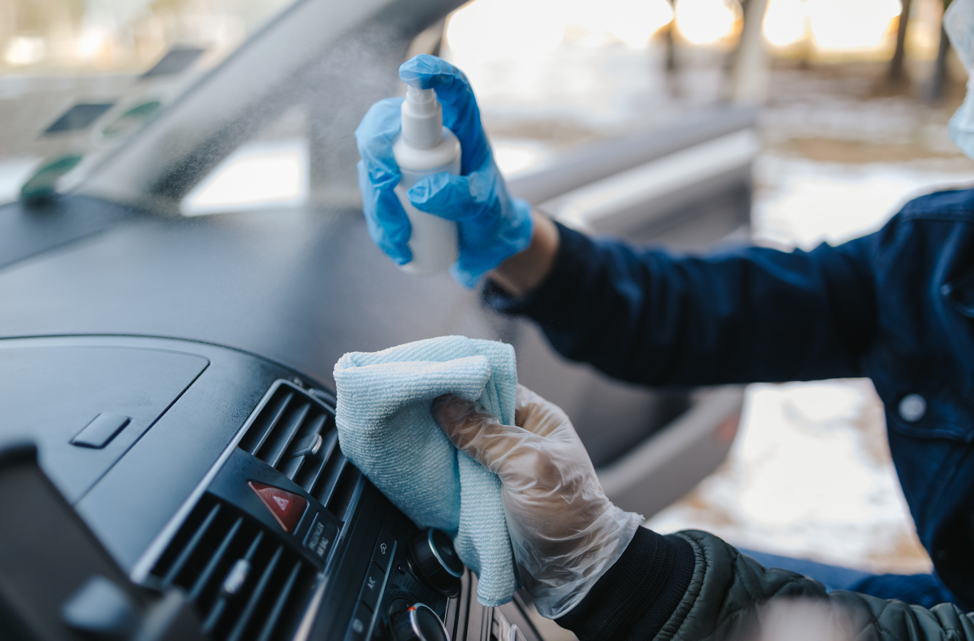 A person wearing gloves and a mask is cleaning the dashboard of a car.