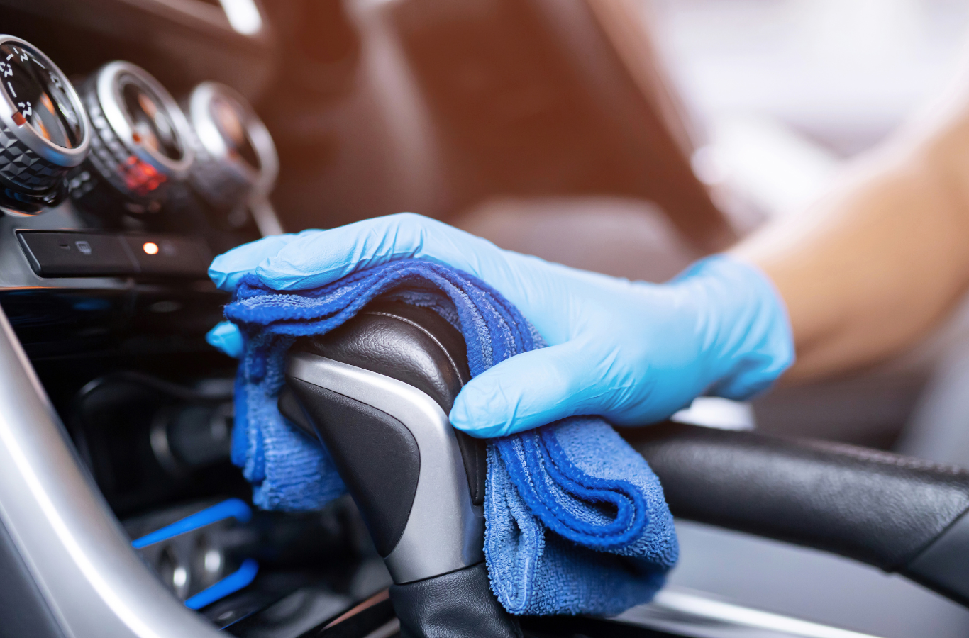 A person wearing blue gloves is cleaning the steering wheel of a car with a cloth.