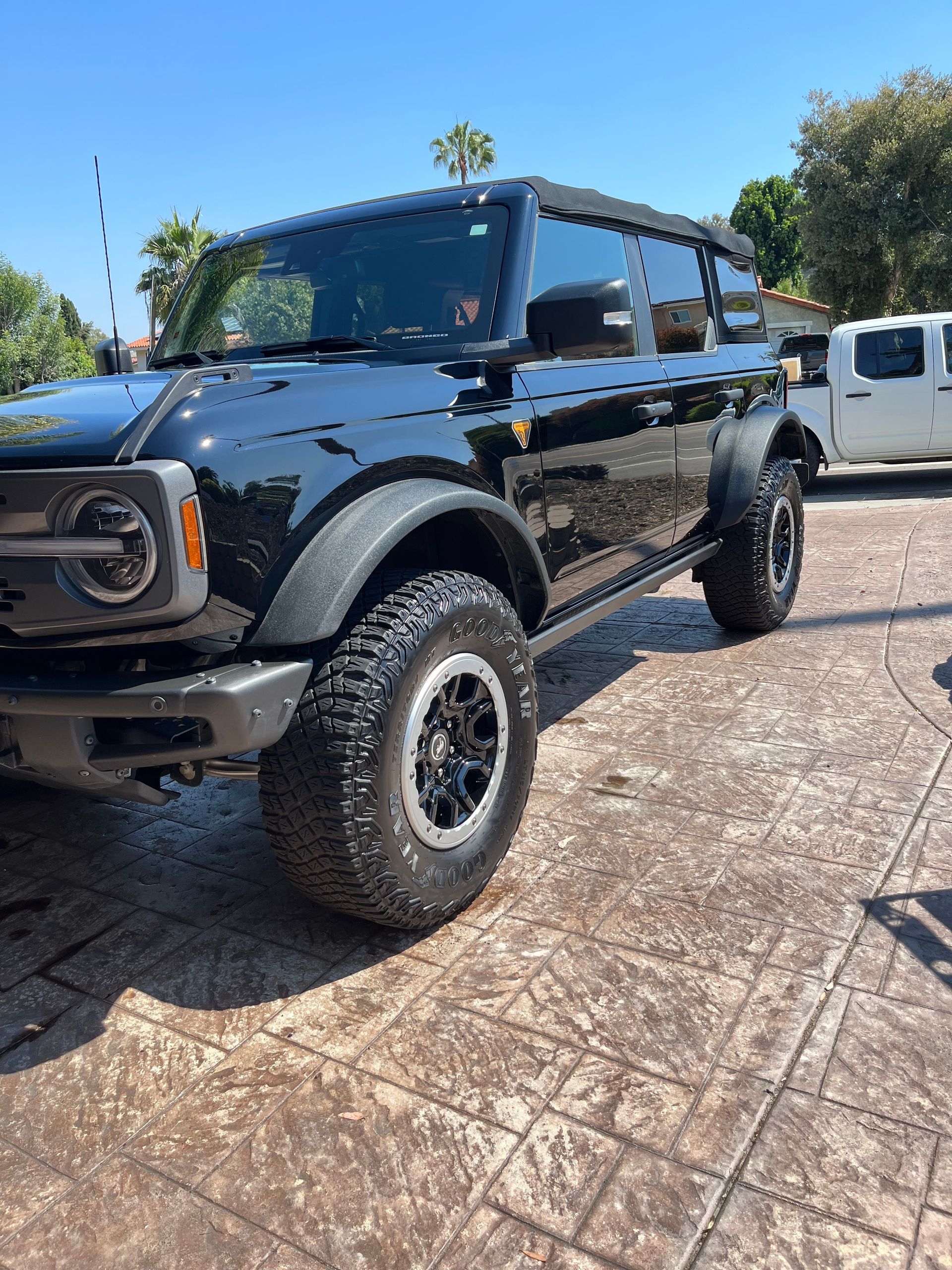 A black ford bronco is parked in a driveway next to a white truck.