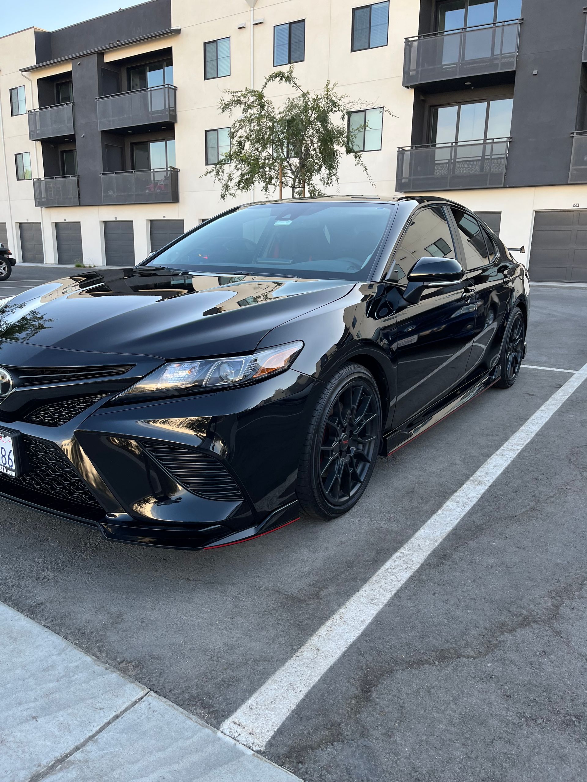 A black car is parked in a parking lot in front of a building.