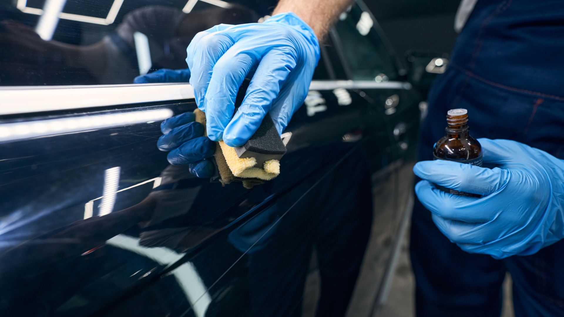 A man wearing blue gloves is polishing a car with a sponge.