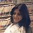 Woman with dark hair smiles, sitting in front of a bookshelf.