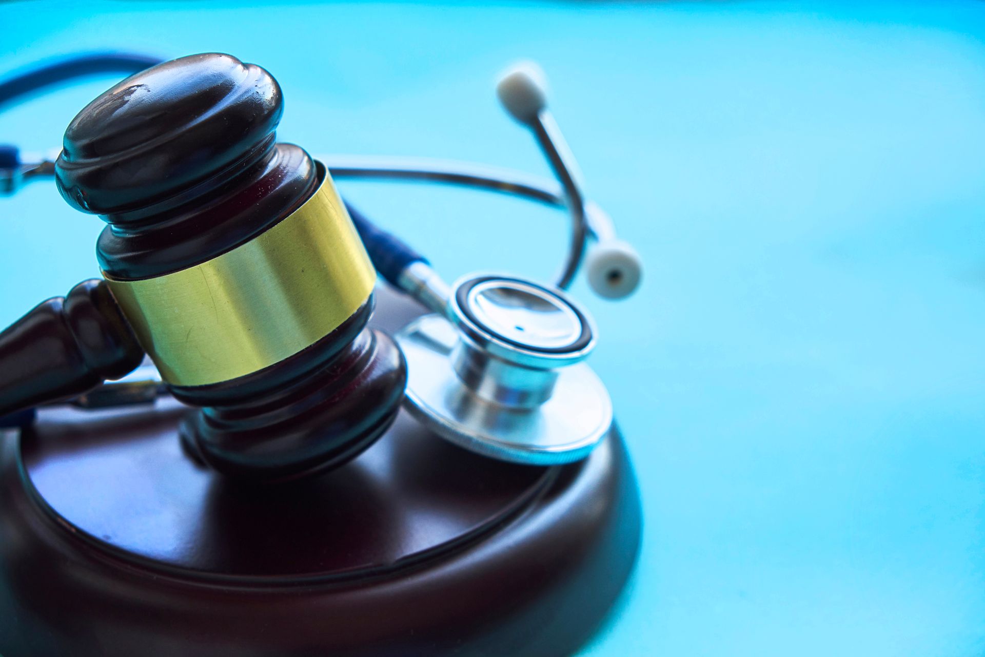 A wooden judge's gavel with a gold band resting next to a silver and black stethoscope on a light blue surface.