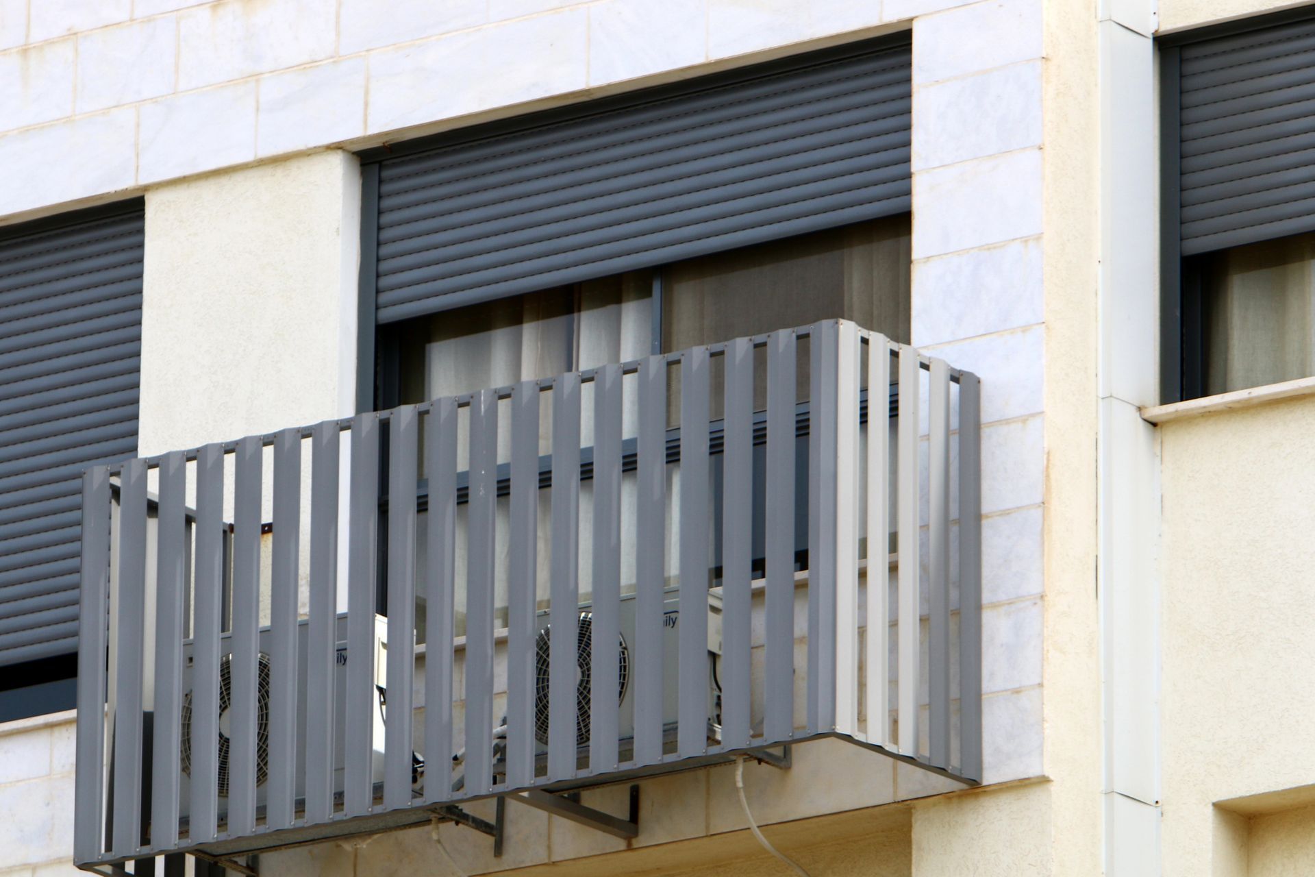 Balcone grigio con lamelle verticali su una facciata beige dell'edificio.