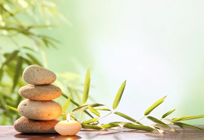 Stack of smooth stones, lit candle, and bamboo sprigs against a soft green background. — Serene Therapy with Lana In Paddington, NSW
