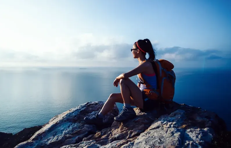 Woman with backpack sits on a cliff, overlooking the sea — Serene Therapy with Lana In Paddington, NSW
