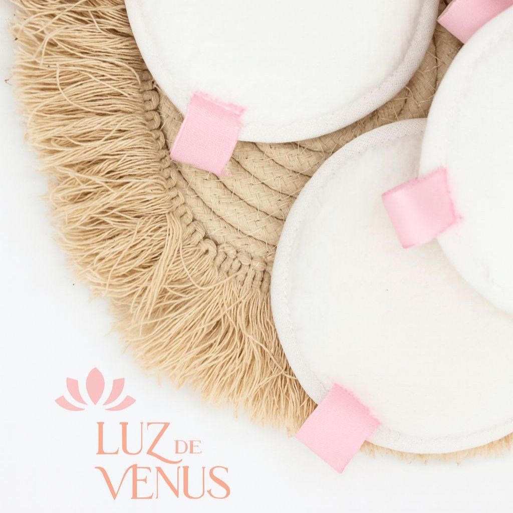 Discos desmaquillantes reutilizables de color blanco con cintas rosas sobre un posavasos de macramé color beige.